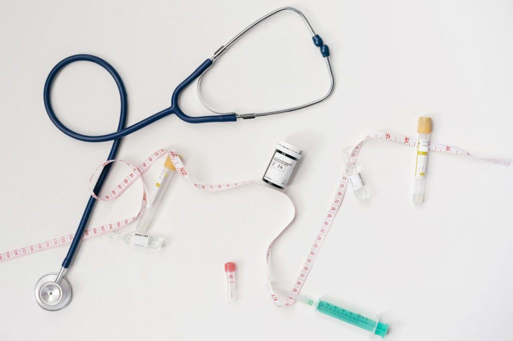Top view of stethoscope, syringes, and tape measure on white background.